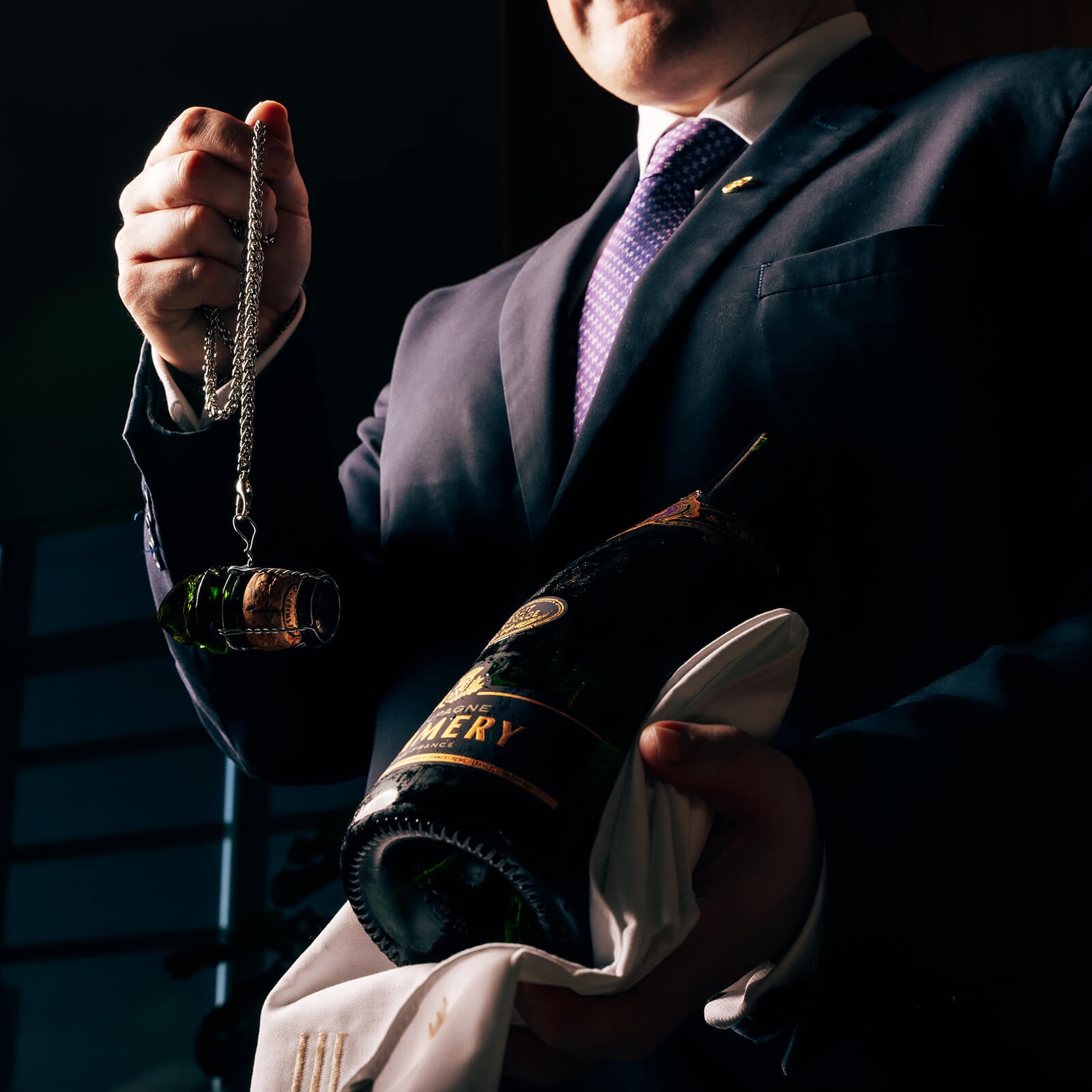 Sommelier holding a champagne bottle after a sabrage strike, with the cork and bottle top secured on a chain for added safety and environmental responsibility.